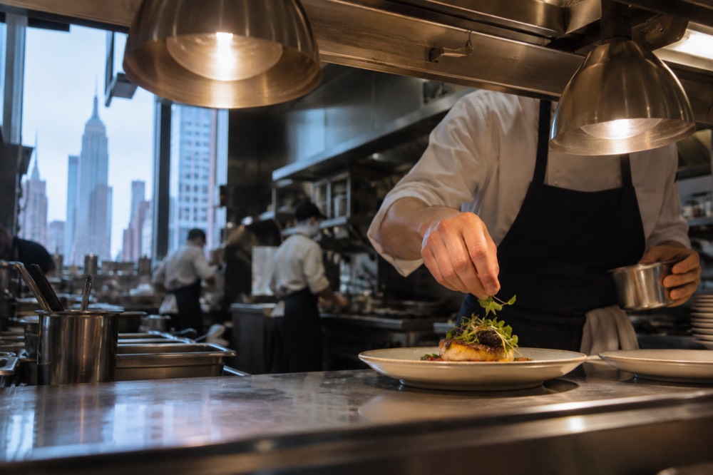 A chef plating a dish at a restaurant pass in a New York kitchen