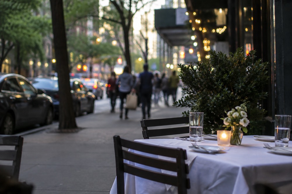 A sidewalk table outside a restaurant on a tree-lined New York street in the evening
