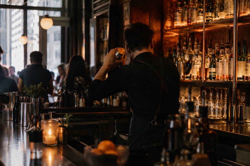 A bartender shaking a cocktail in front of a dim copper bar