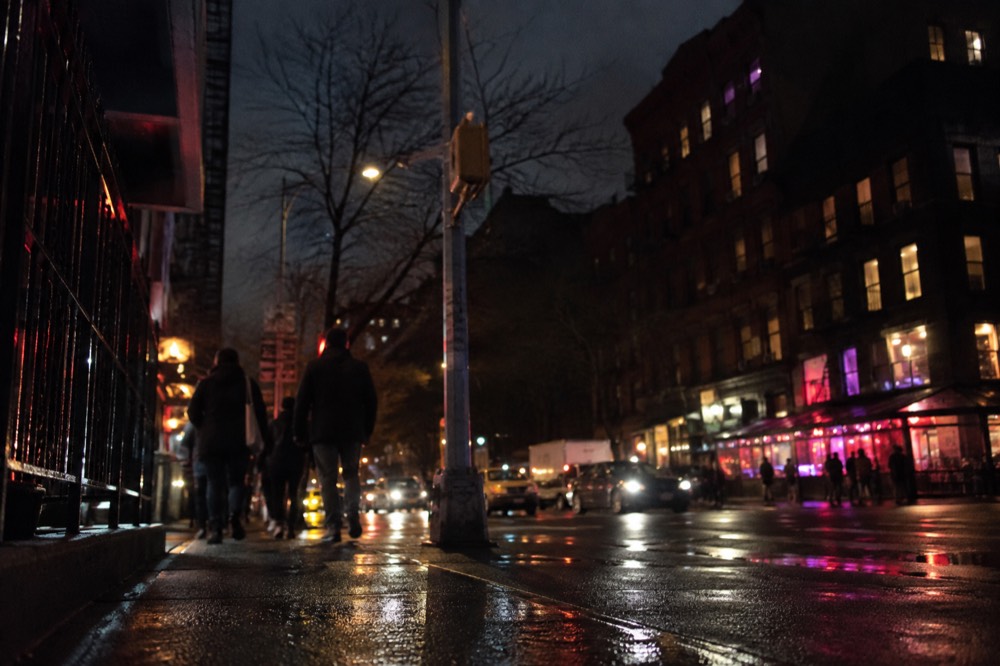 A nighttime street corner in the East Village with neon shop signs