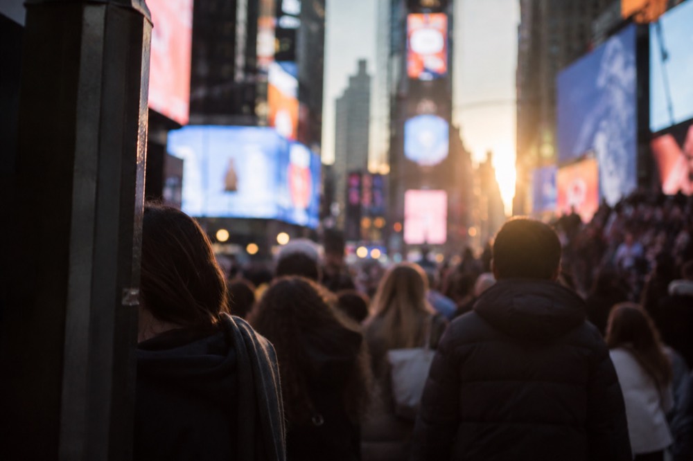 A crowded Times Square at dusk with billboards lit and pedestrians crossing