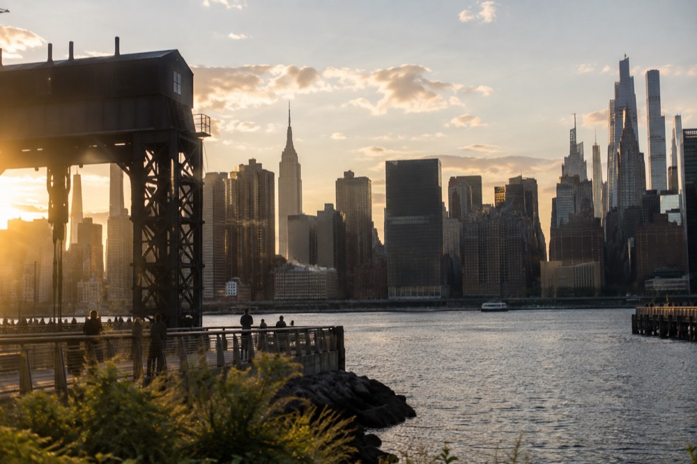 The Manhattan skyline seen across the East River from a waterfront park with old gantry cranes