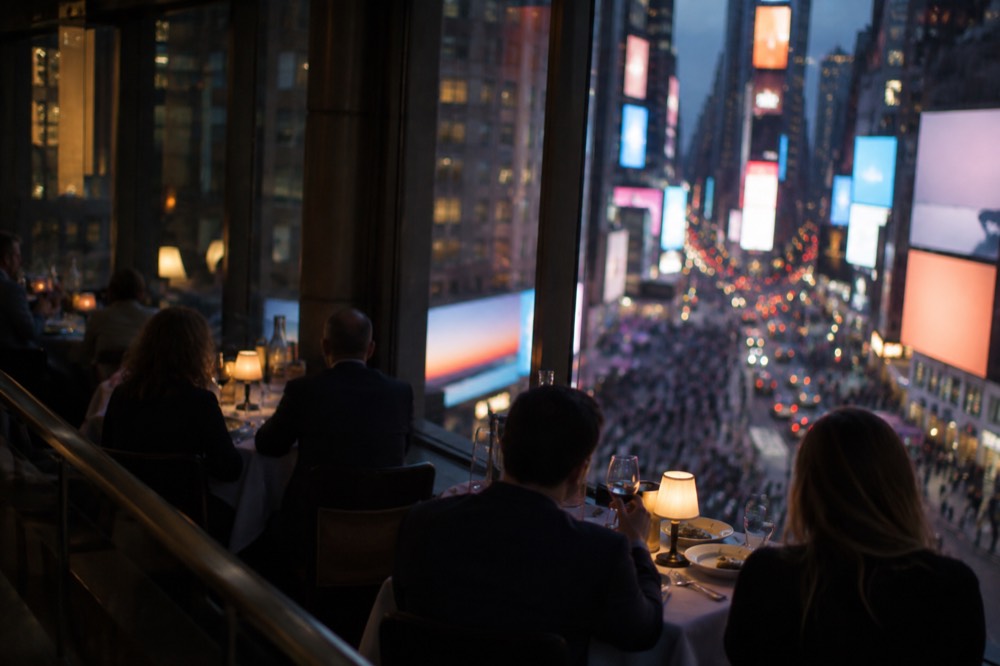 A restaurant table with pre-theatre diners and theatre district lights visible through the window