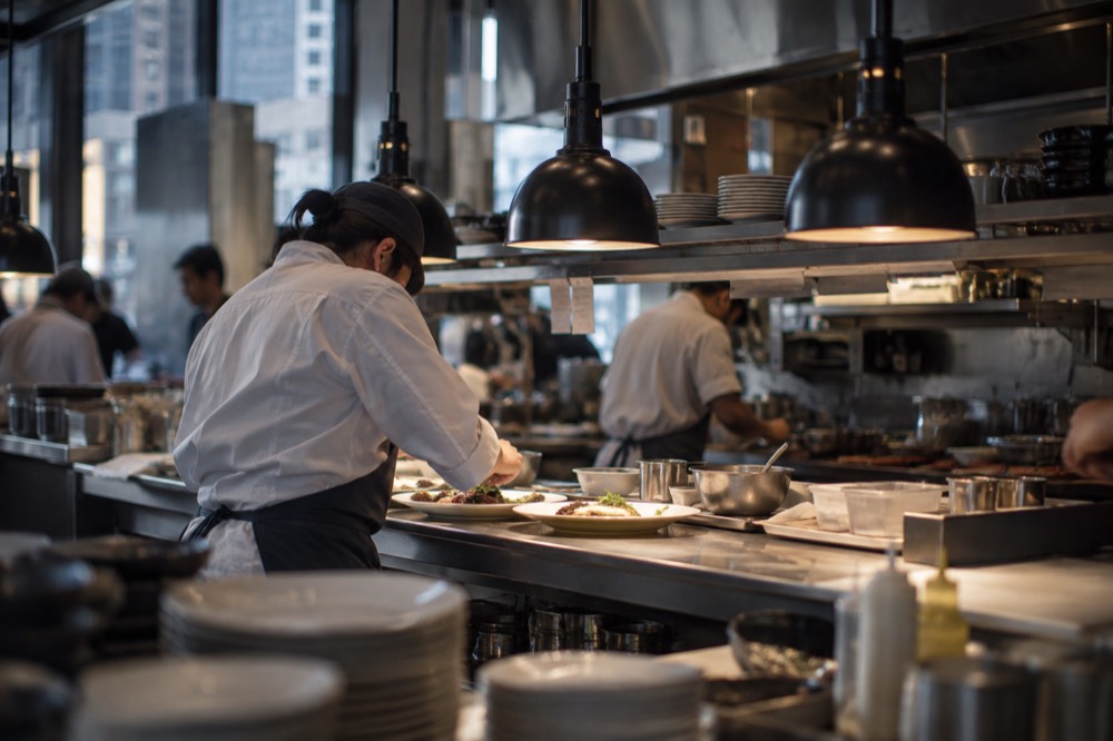 A chef plating a dish at a busy open kitchen pass in a Manhattan restaurant