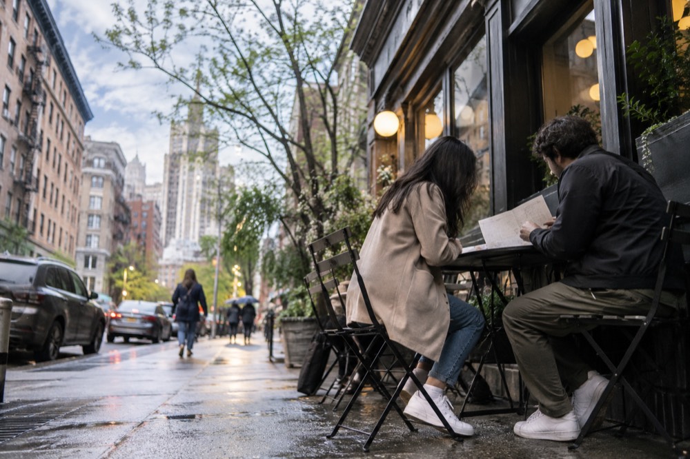 A couple reviewing a printed itinerary at a cafe table in a Manhattan neighborhood