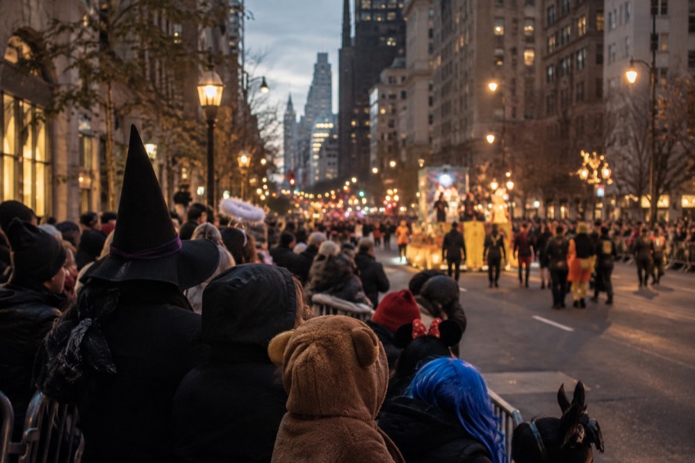 Spectators in costume lining a lamplit avenue waiting for a night parade