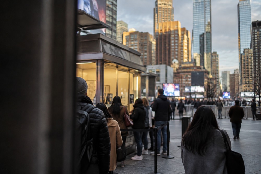 People queuing at an outdoor discount ticket booth in a Midtown plaza under a gray sky