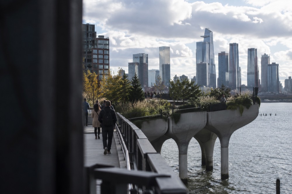An elevated park on concrete pilings above the Hudson River with green paths and people strolling