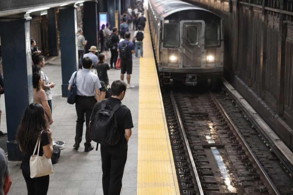 A subway platform with a train arriving and passengers waiting behind the yellow line