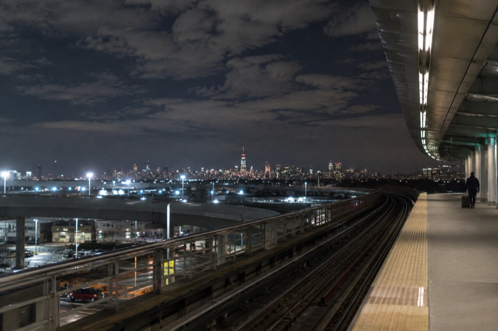A nearly empty AirTrain platform at JFK late at night with the Manhattan skyline far in the distance