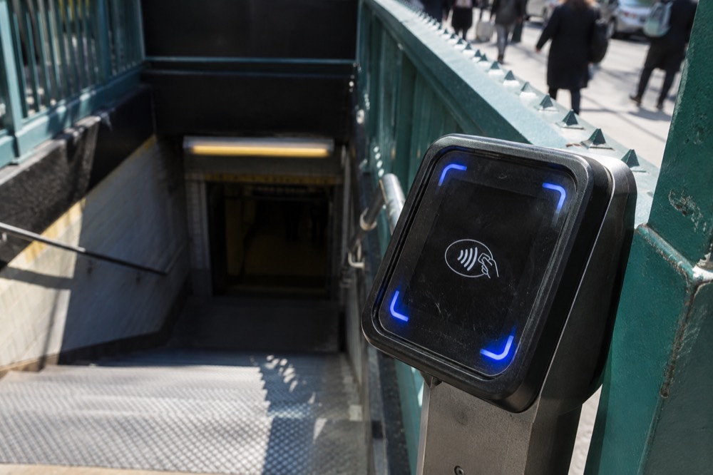 A close-up of an OMNY tap reader showing the contactless payment symbol at a New York subway entrance