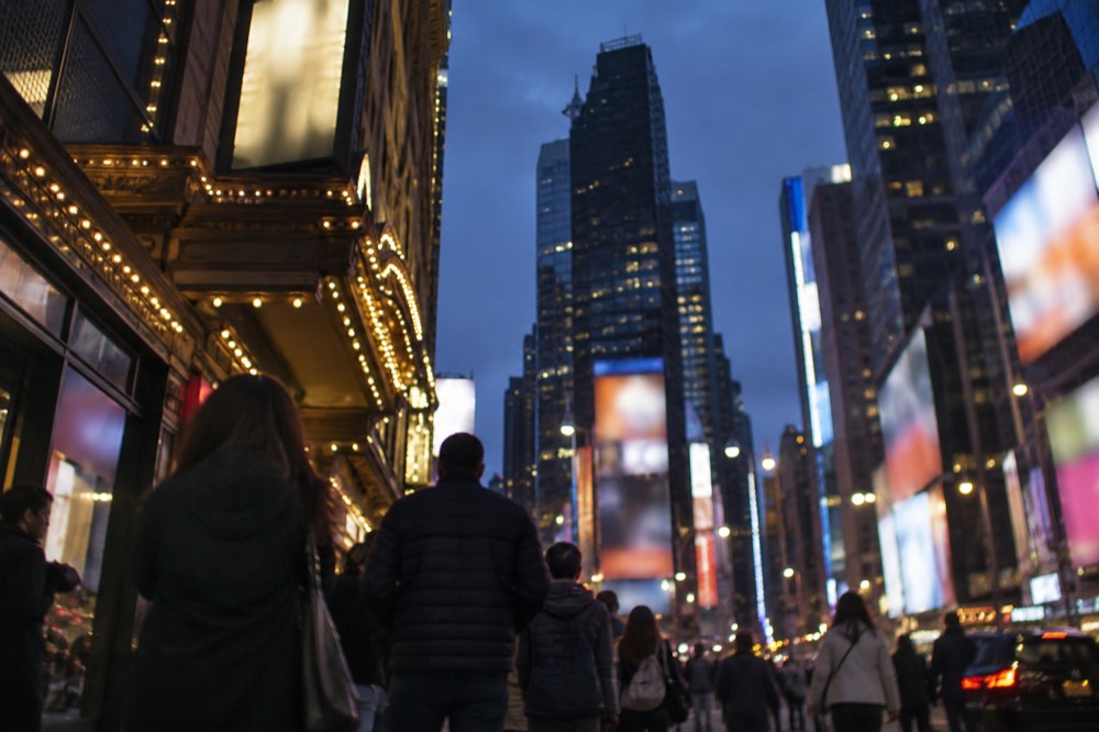 A busy Times Square sidewalk at night with theatre posters and glowing billboards