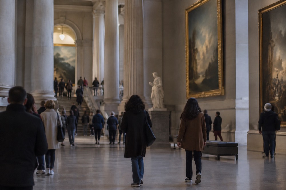 Visitors walking through a grand museum hall with marble columns and large paintings
