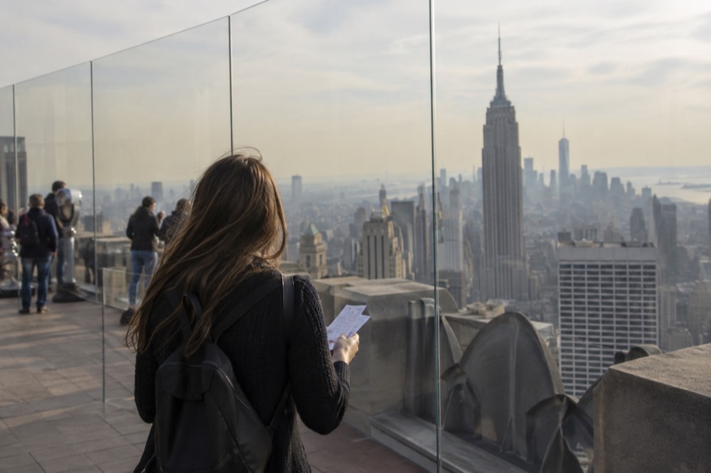 A tourist holding attraction tickets while looking at a Manhattan skyline viewpoint