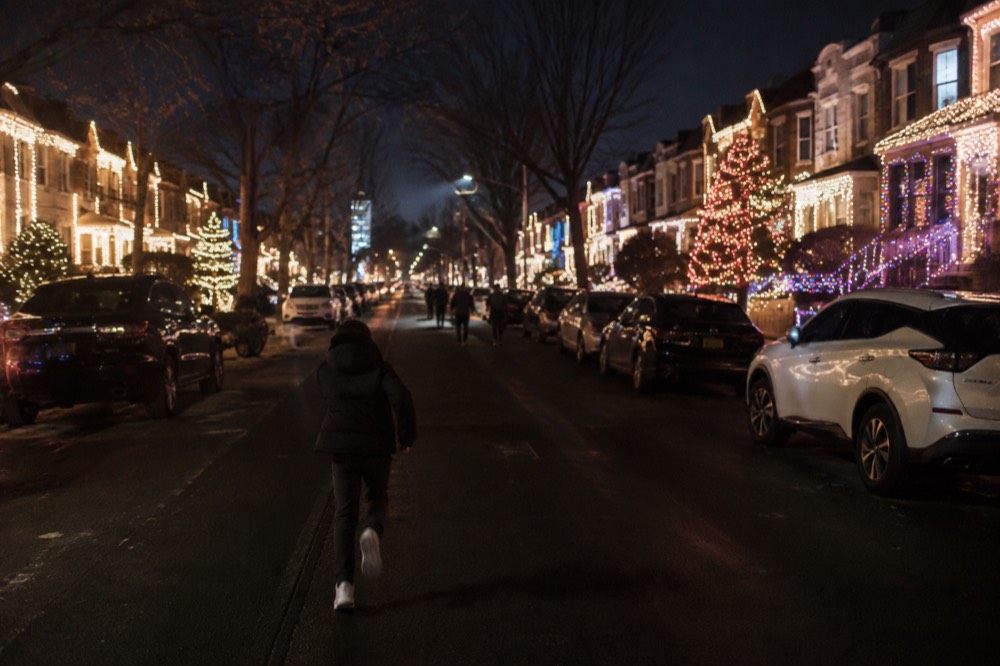 A wide Brooklyn street at night with rows of houses glowing with elaborate holiday light displays