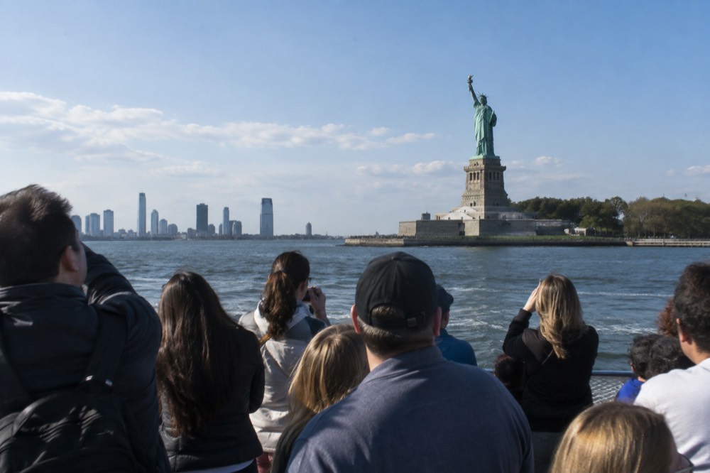 Ferry passengers on the open deck of a boat approaching the Statue of Liberty in New York Harbor