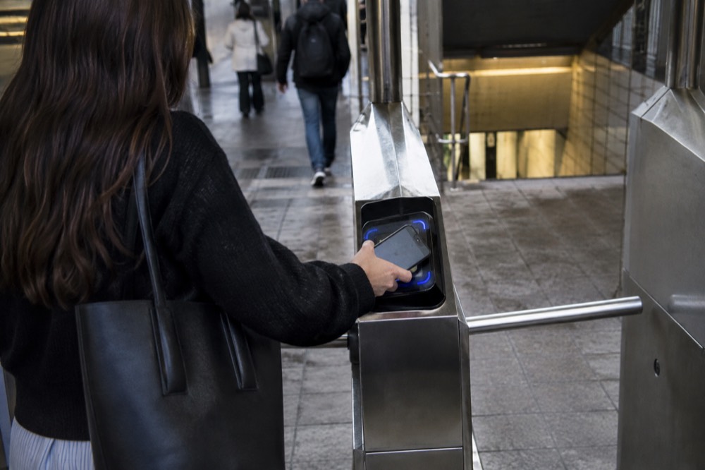 A visitor tapping a phone on an OMNY reader at a subway turnstile