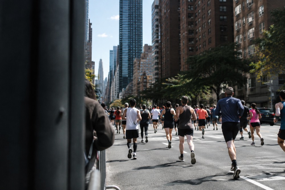 A wide city avenue filled with runners between tall apartment buildings