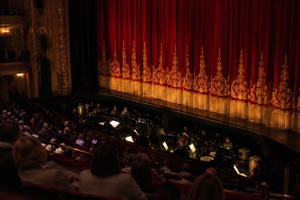 The stage curtain and orchestra pit of a Broadway theater lit for an evening performance