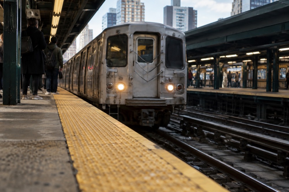 A New York subway platform with a silver train arriving behind yellow safety stripes