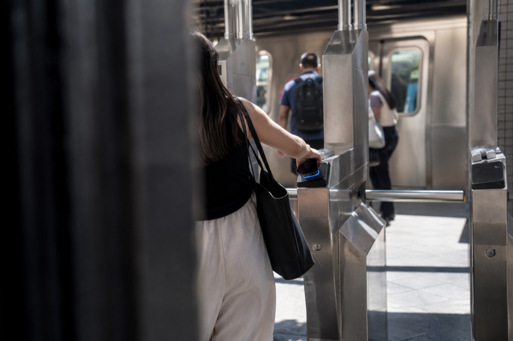 A passenger tapping a phone on an OMNY reader at a subway turnstile