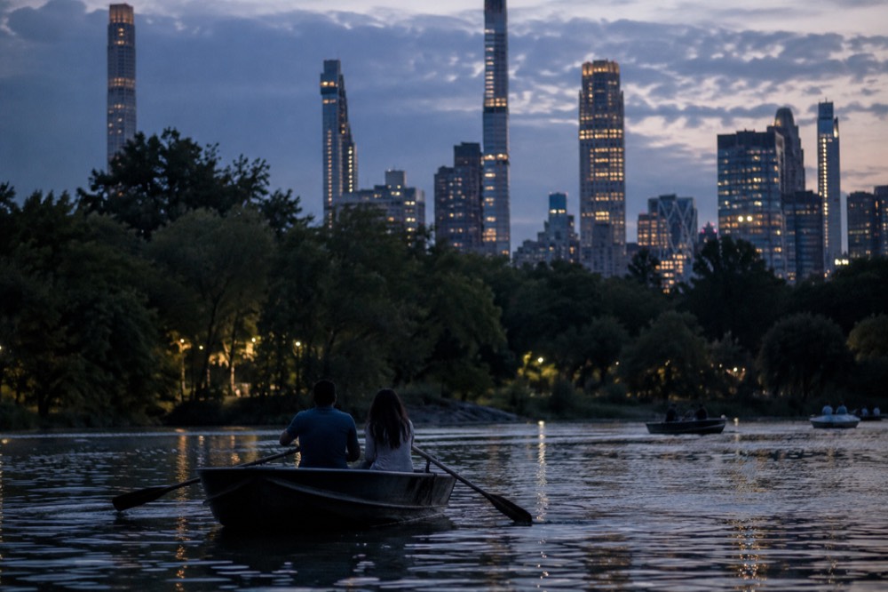 People rowing a rowboat on a lake with trees and buildings behind