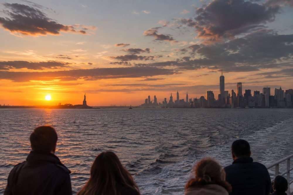 The Manhattan skyline seen from a boat on the harbor at sunset, with the Statue of Liberty in the distance