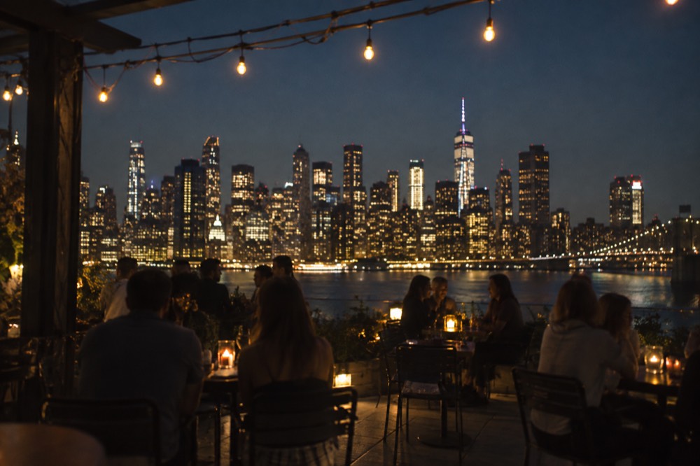 A Brooklyn rooftop bar at night with the Manhattan skyline lit up across the East River