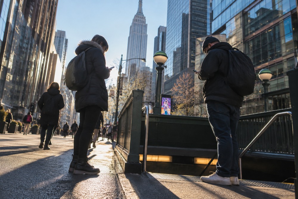 Two travelers checking phones at a subway entrance in Midtown Manhattan