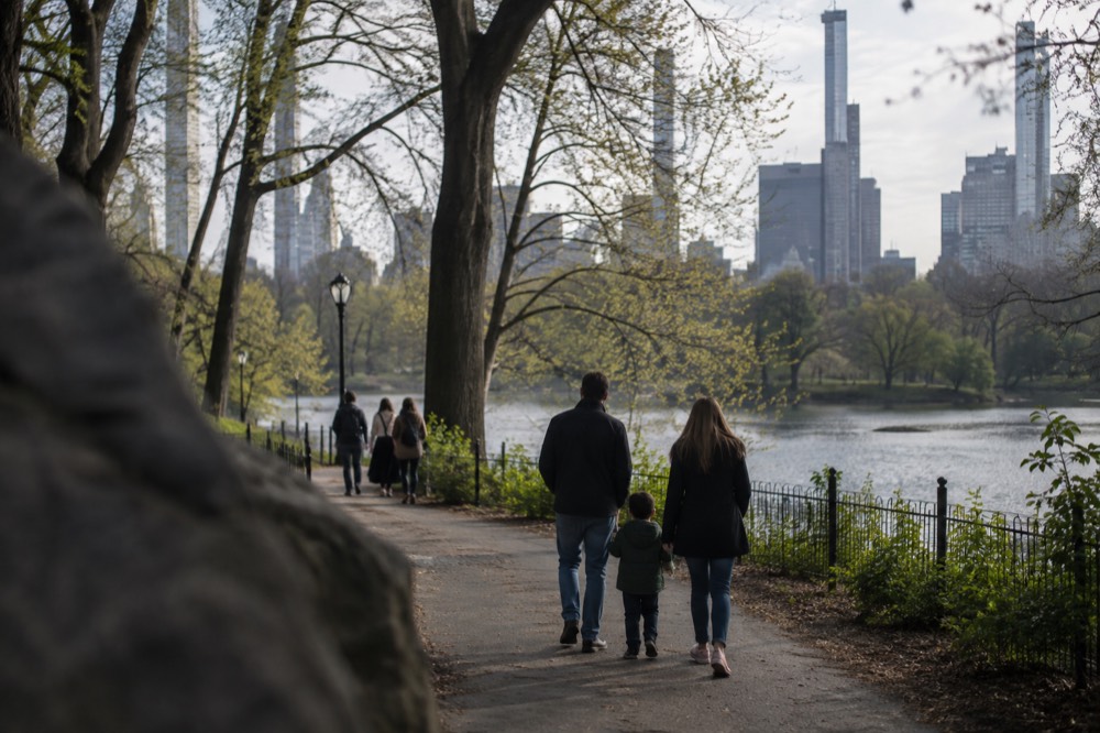 A family walking along a park path with tall trees and a lake in the background