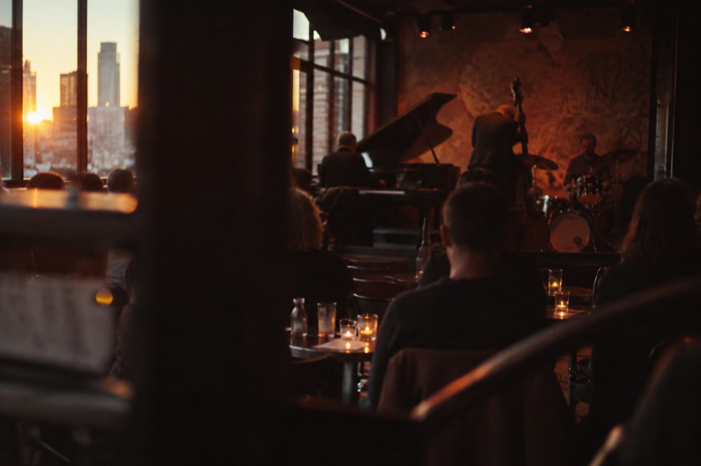 A small jazz club interior with a band performing under warm stage lights and patrons seated at tables