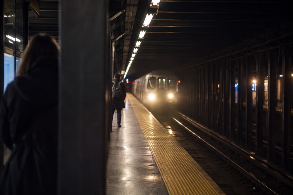 An empty subway platform at night with a train arriving and its headlights visible down the tunnel
