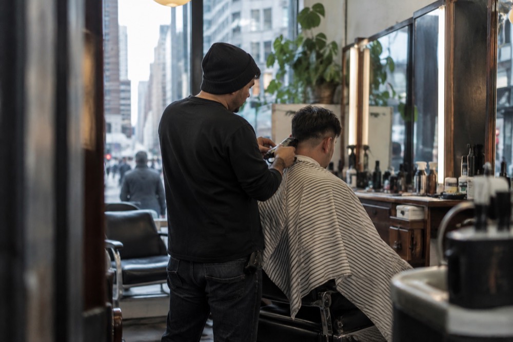 A barber trimming a customer's hair in a small New York barbershop