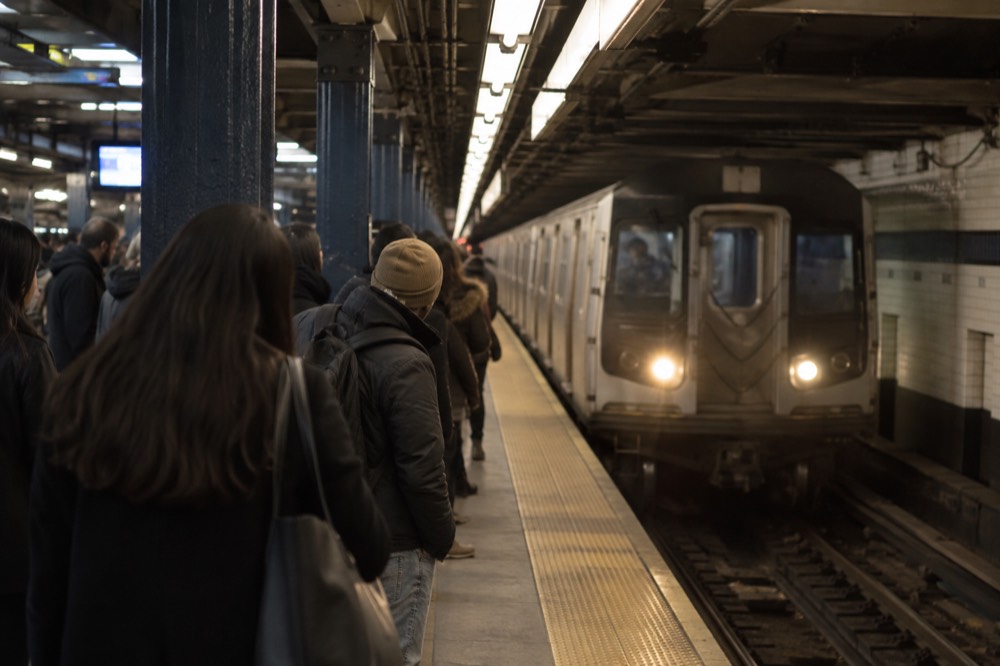 A crowded Manhattan subway platform with a train arriving