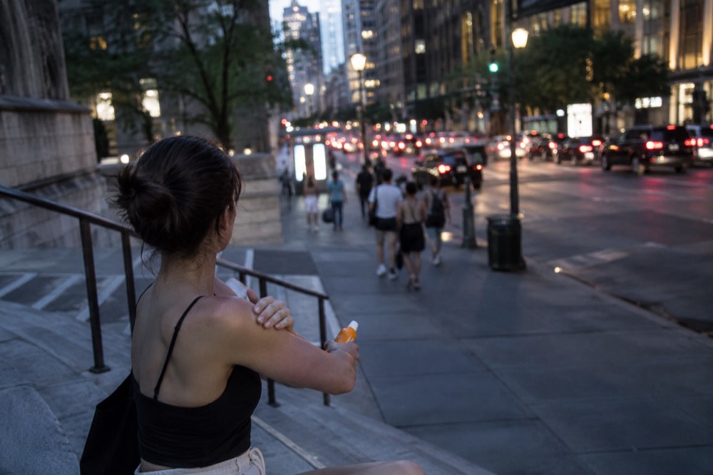 A person in summer clothing applying sunscreen on a sunny New York street