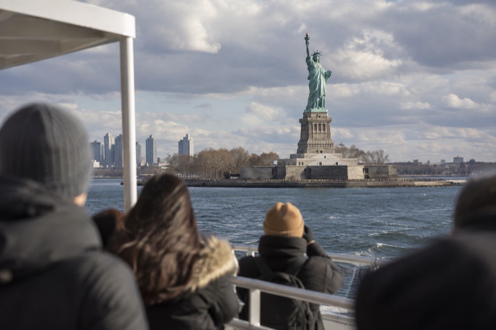 The Statue of Liberty seen from a ferry on the water, with visitors on deck.