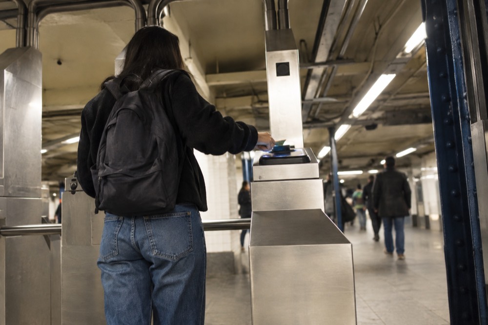 A traveler with a small backpack tapping a contactless card at a subway turnstile in a tiled station