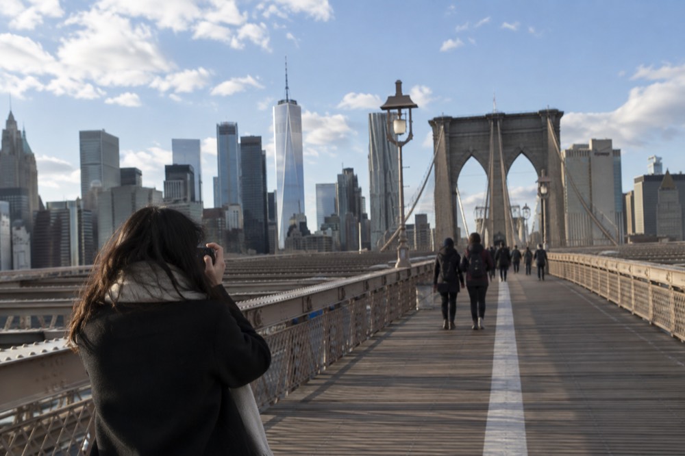 A visitor photographing the Brooklyn Bridge promenade on a clear morning