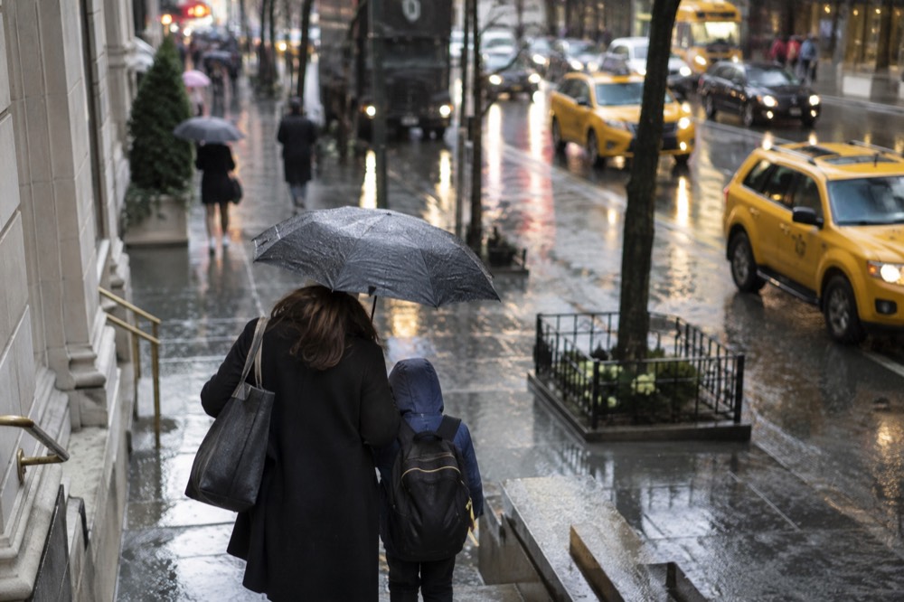A parent and child sharing an umbrella on a rainy city sidewalk with yellow taxis passing